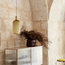 Vitrina baja de acero y cristal estriado de Ferm Living, acero beige: vitrina beige junto a un muro de piedra con jarrón de ramas.