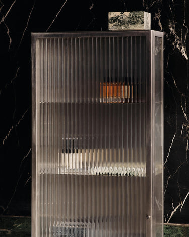 Vitrina de Ferm Living: detalle de vitrina con frascos sobre pared oscura veteada.