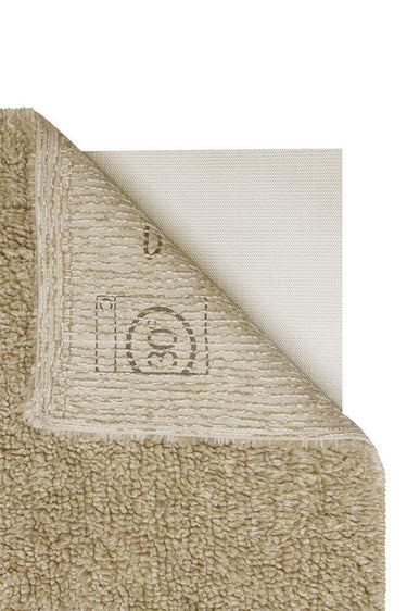 Alfombra Tundra beige de 80 × 140 cm junto a una cama